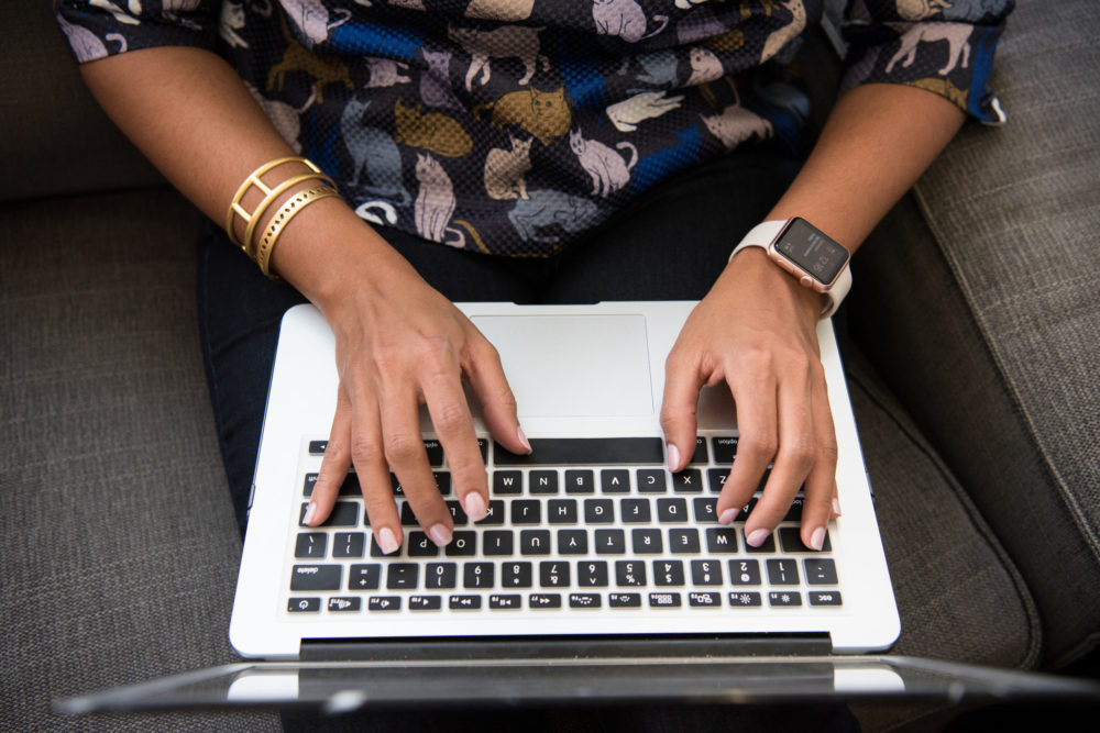 hands typing on a Mac keyboard. left hand has an Apple watch, right hand has two bracelets. 
