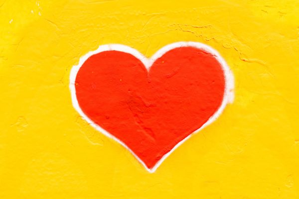 A Red heart, outlined in white on a yello background