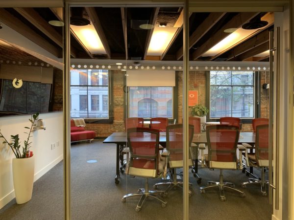 Image of a conference room with chairs, lights, a table, a plant, and a large TV.