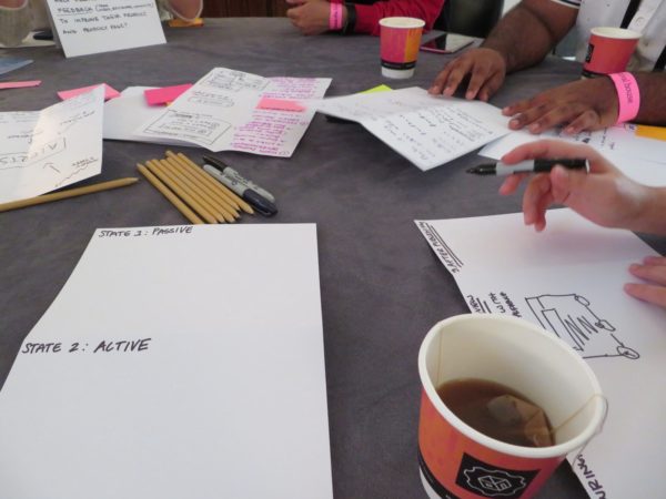Image shows hands, paper, pencils, cups of coffee and tea.
