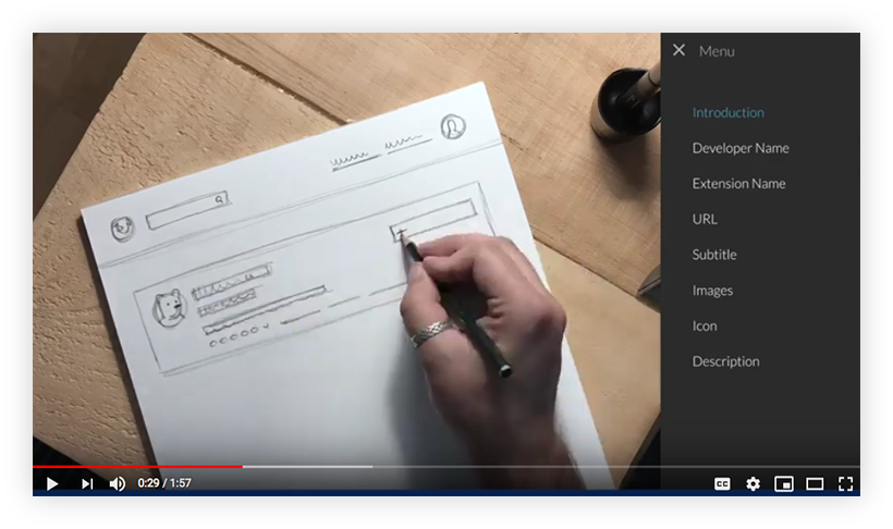 Screenshot of a video. A hand is sketching a rough product page on a piece of paper. Next to the paper is a table of content that includes an introduction and the main content elements on a product page, such as Developer Name, Extension Name, etcetera.