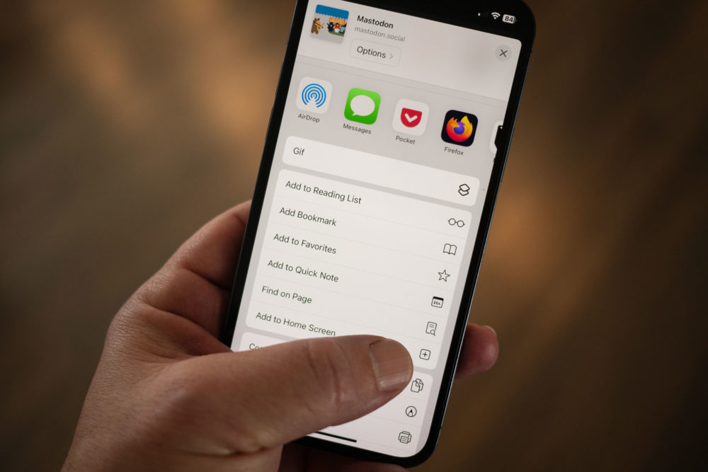 An iPhone in hand with the thumb near the Add to Home Screen item in the share menu.