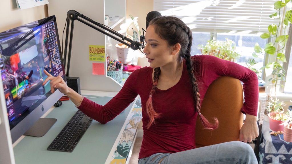 Xyla Foxlin, sitting in front of a computer, points at a video playing on a monitor.