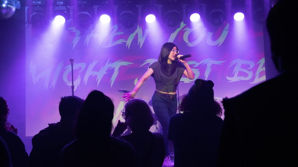 LEX the Lexicon Artist raps on stage holding a mic in front of a crowd.