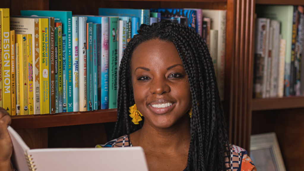 Charnaie Gordon holds up a book in front of a bookshelf. 