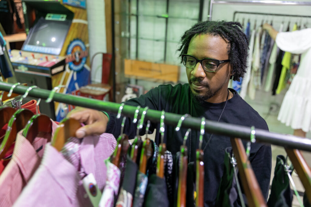 A man smiles while sorting through clothes on a rack inside the store.