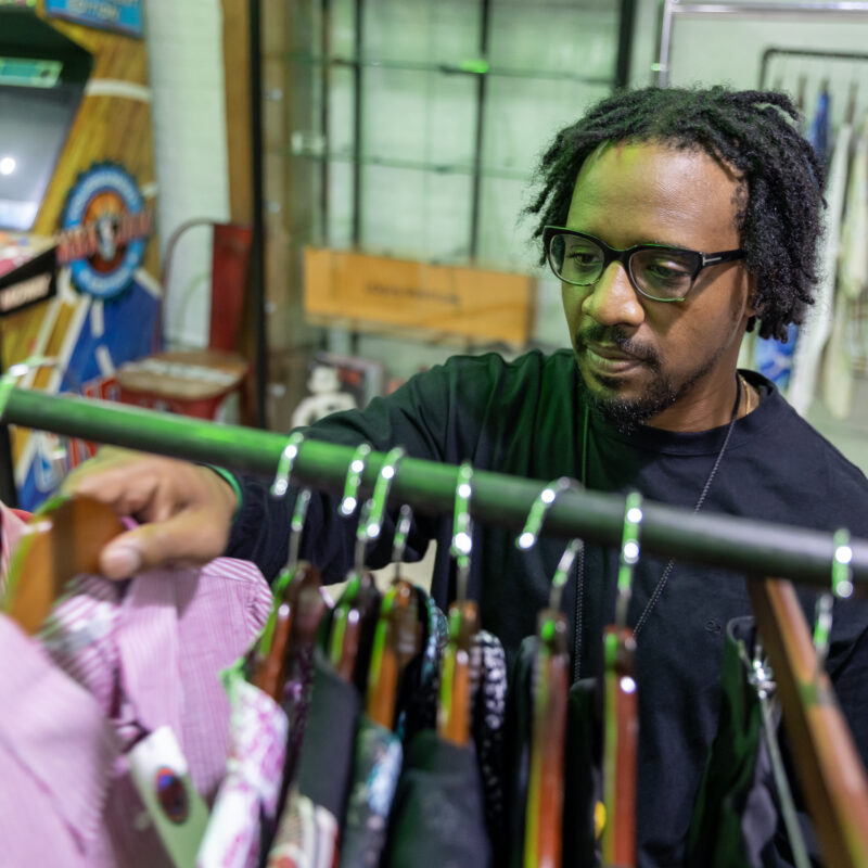 A man smiles while sorting through clothes on a rack inside the store.