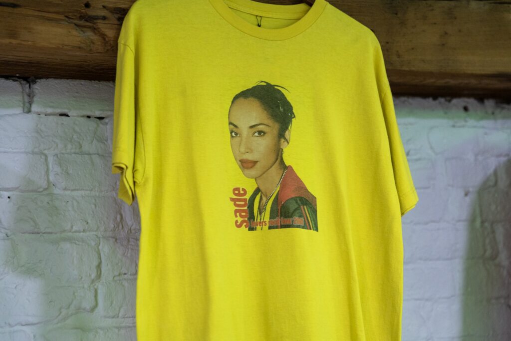 Yellow Sade t-shirt from the Lovers Rock Tour hanging against a white brick wall.