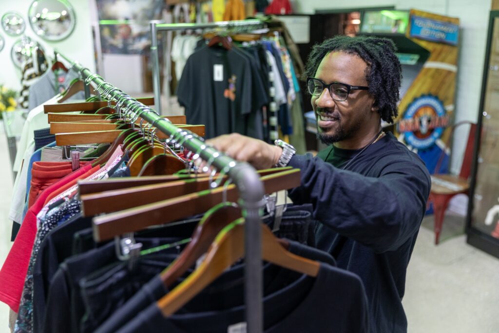 A man smiles while sorting through clothes on a rack inside the store.