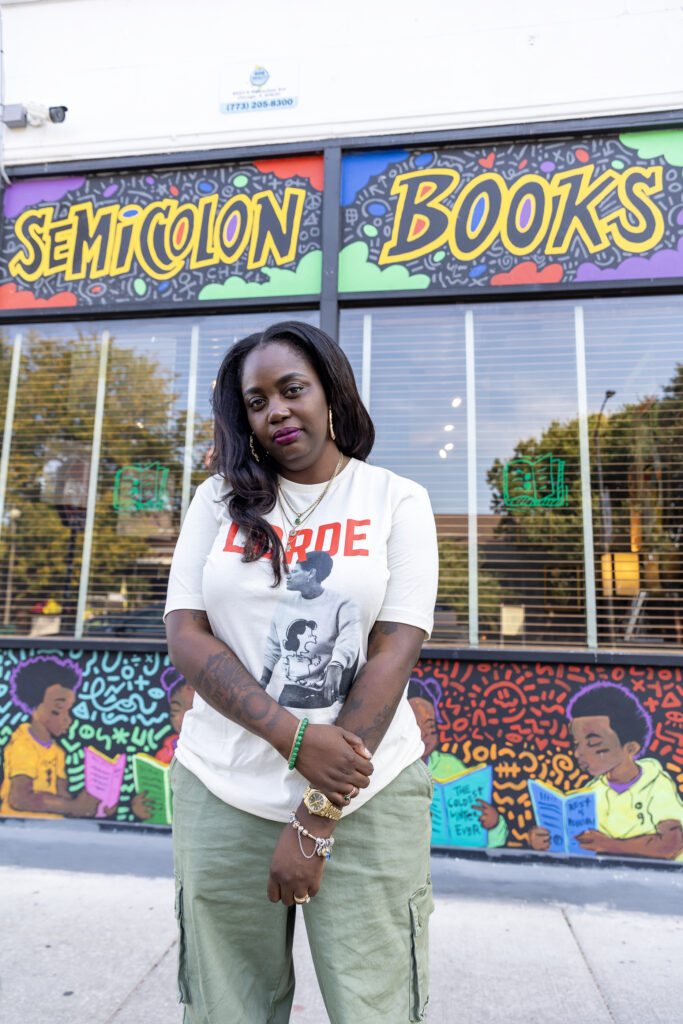 A woman stands confidently in front of Semicolon Books, wearing a Lorde t-shirt, with the vibrant storefront and mural behind her.