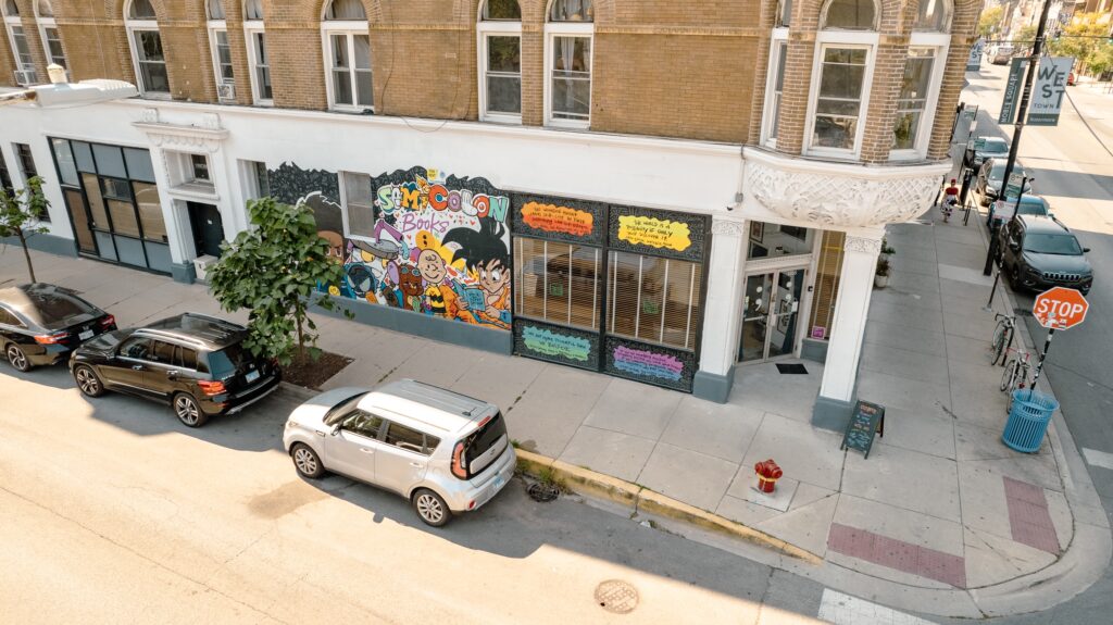 Aerial view of Semicolon Books, showing the storefront with a colorful mural and several parked cars along the street.