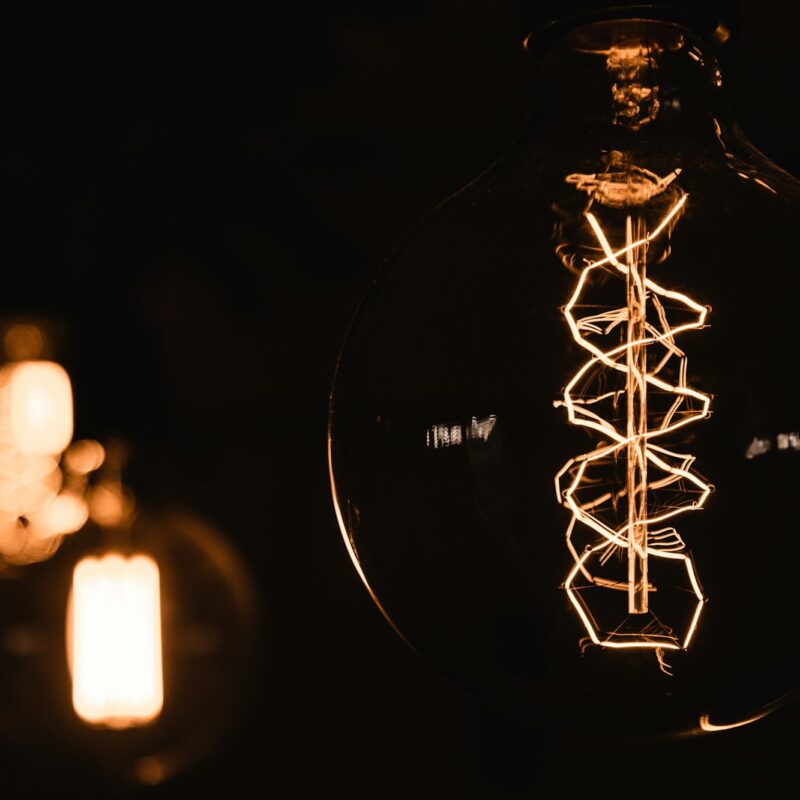 Close-up of a glowing vintage-style lightbulb with intricate filament design, against a dark background.