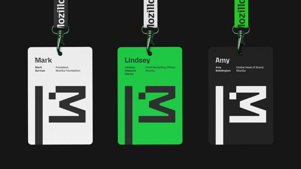 A set of three ID badges with minimalist designs, each featuring a stylized black flag logo, a name, title, and Mozilla branding on green, black, or white backgrounds. The lanyards have "Mozilla" printed in bold text.