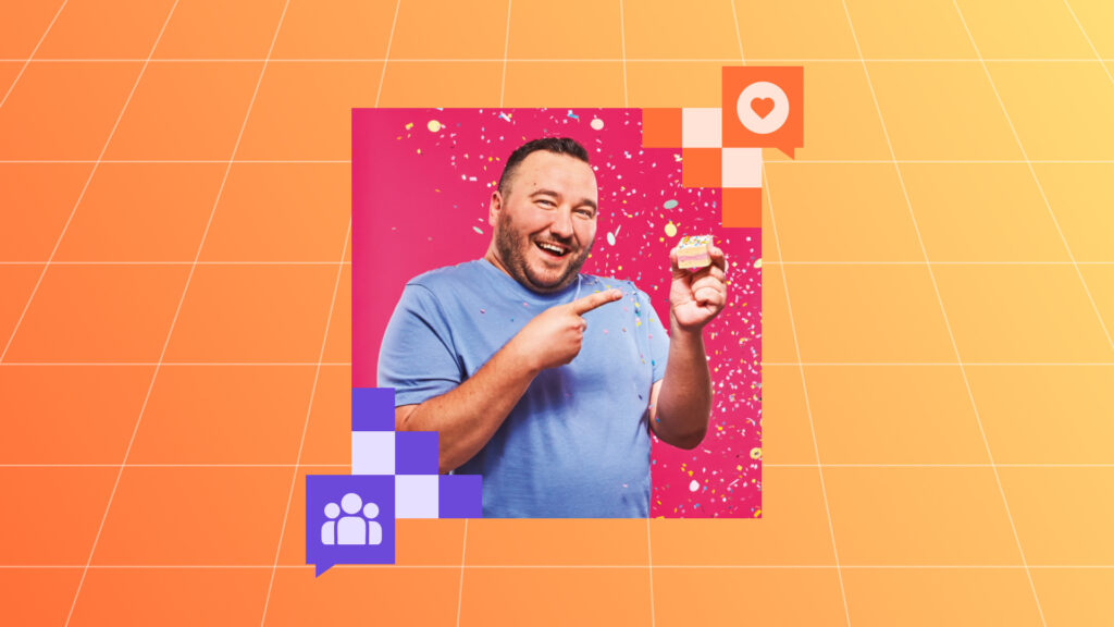 A smiling man in a light blue shirt stands in front of a bright pink background, surrounded by colorful confetti. He’s pointing enthusiastically at a small, square sprinkle-topped cake he’s holding in one hand.