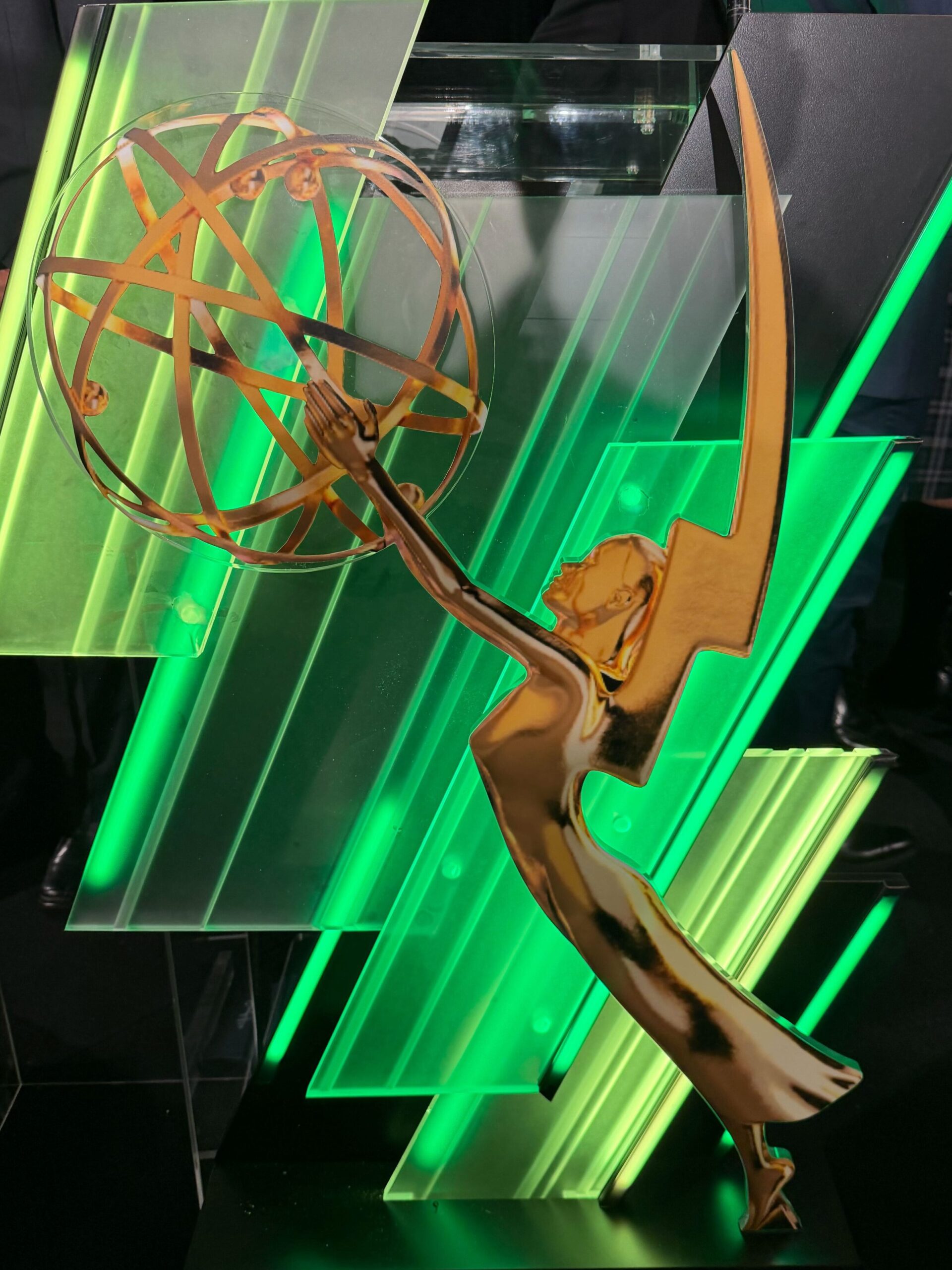 Gold Emmy-style statuette in front of green illuminated panels at an award ceremony podium.